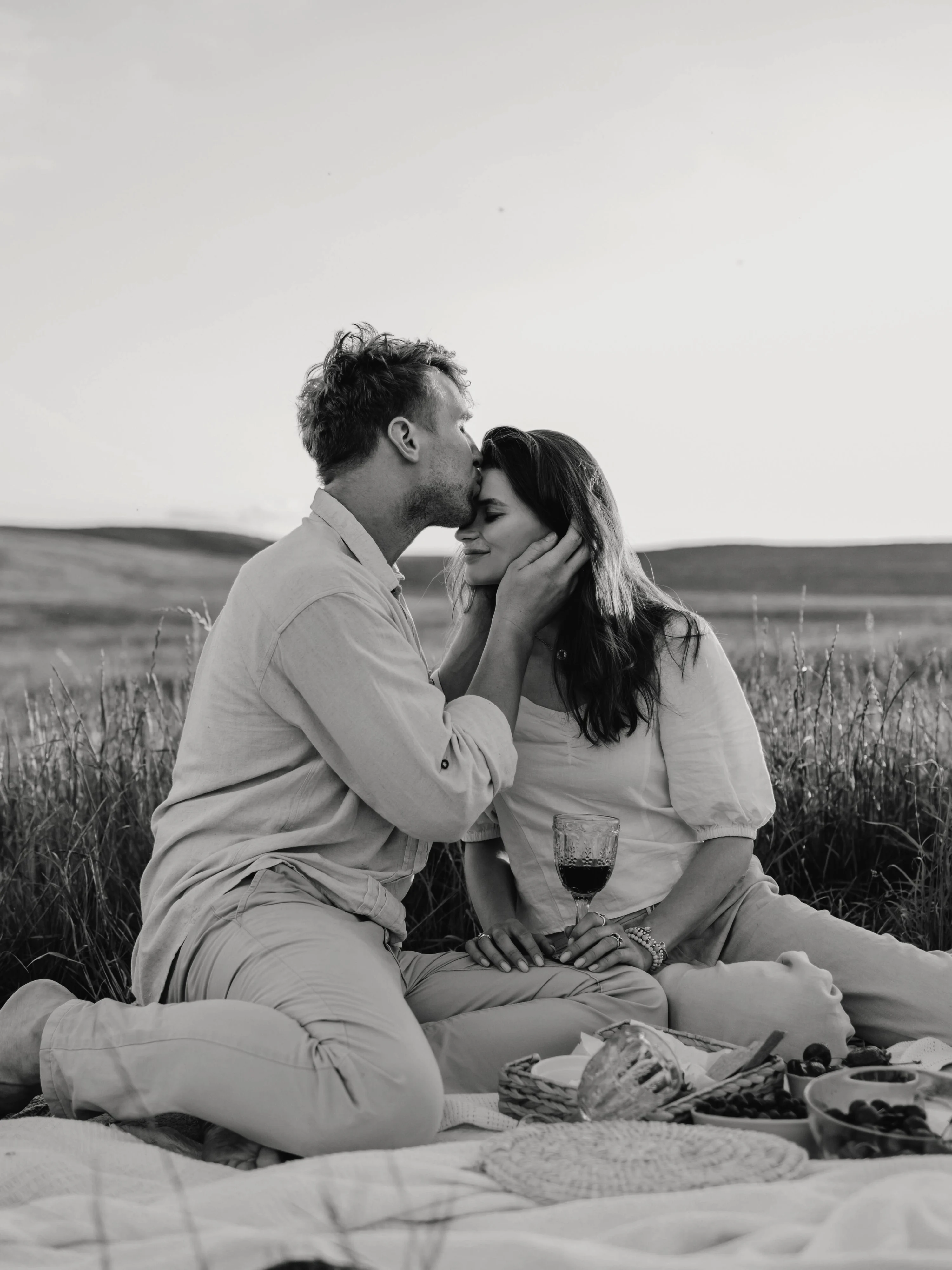 Renata y Andrés en un picnic en el campo; él la besa en la frente